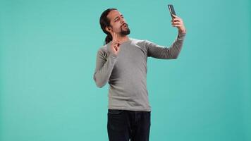 Man using smartphone to take selfies and post them on social media, studio backdrop. Vain person taking photos using phone selfie camera, isolated over studio background, camera A video