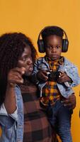 Vertical Joyful optimistic dad playing online games with his boy using controller, parents enjoying leisure time with their small child. African american happy family play together in studio. Camera B. video