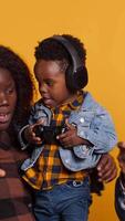 Vertical Joyful optimistic dad playing online games with his boy using controller, parents enjoying leisure time with their small child. African american happy family play together in studio. Camera A. video