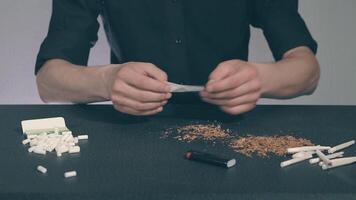 Man in Black Clothing is Rolling a Hand Made Cigarette Using Papers, Filters and Tobacco. A Way to Save on Tobacco Products. Tobacco Product Economy Concept video