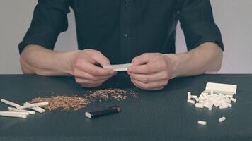 Man in Black Clothing is Rolling a Hand Made Cigarette Using Papers, Filters and Tobacco. A Way to Save on Tobacco Products. Tobacco Product Economy Concept video