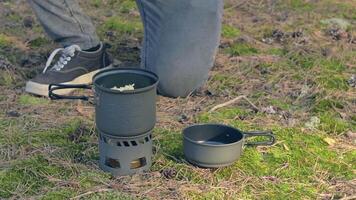 uomo nel un' foresta è cucinando pasta utilizzando un' piccolo cucinare impostare. escursionista nel un' foresta è preparazione per il il pranzo. statico avvicinamento tiro video