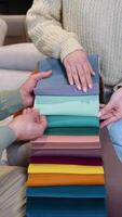 A man and woman choosing upholstery fabric color and texture from various colorful samples for sofa in a store. Vertical video