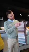 A man choosing upholstery fabric color and texture from various colorful samples for sofa in a store. Vertical video