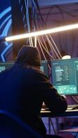 Vertical Skilled hacker deploying malware on unaware victims computers, stealing sensitive and private information, selling on darknet to highest bidder, looking at computer screen in hideout, camera A video