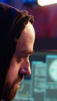 Vertical Hooded hacker targeting vulnerable unpatched connections, seeking to compromise digital devices and steal valuable sensitive data. Evil man running code in graffiti painted basement, camera B close up video