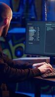 Vertical Hacker listens music while hiding in underground bunker and coding, stealing data from victims using PC virus. Rogue programmer wearing headphones tricks people into installing ransomware, camera B video