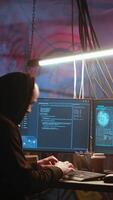 Vertical Hacker arrives in messy base of operations with neon lights and graffiti drawings sprayed on walls. Cybercriminal using ghetto hideout as HQ to commit illegal activities using computer, camera B video