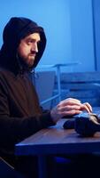 Vertical Hacker listens music while hiding in underground bunker and coding, stealing data from victims using PC virus. Rogue programmer wearing headphones tricks people into installing ransomware, camera A video