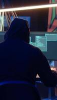 Vertical Hooded man in underground hideaway utilizing technical knowhow of bugs and exploits to break into computer systems and access valuable data, bypassing firewalls and login process, dolly in shot video
