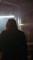 Vertical Hacker using software interface on computer screen, running programming code in warehouse with graffiti sprayed on walls. Evil developer in underground base building malware, handheld camera shot video