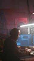Vertical Hacker running phishing software on computer in criminals den with graffiti sprayed on walls. Cybercriminal doing malware programming in dark foggy underground base, breaching security video