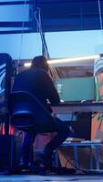 Vertical Hooded hacker leaving neon lit underground shelter after launching DDoS attack on websites. Cybercriminal finishing work on script that can crash businesses servers, exiting headquarters, camera A video