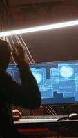Vertical Hacker in dark neon lit underground HQ coding malware designed to exploit network backdoors, using tools to bypass security measures such as logins and password protections. handheld camera shot video