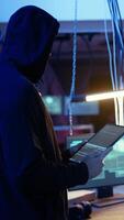 Vertical Lone wolf hacker in neon lit secret hideout trying to hide his online activity after stealing data from victims using computer virus, trying to avoid being detected, using tablet, camera A video