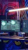 Vertical Zoom in shot of abandoned basement with graffiti drawings on walls and advanced technology computers left open running code. Underground hideout painted in grungy style used by hackers video