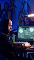 Vertical Skilled hacker deploying malware on unaware victims computers, stealing sensitive and private information, selling on darknet to highest bidder, looking at computer screen in hideout, camera B video