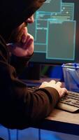 Vertical Hacker hiding in underground bunker, chatting with friend in telephone call, anxious after stealing data from victims using computer virus, scared about being caught by police, camera B close up video
