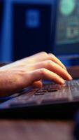 Vertical Hacker in secret underground shelter typing on keyboard, writing lines of code on computer, trying to get past security systems with virus. Scammer working on hacking script, camera A close up shot video