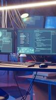 Vertical High tech computer system running malicious code in empty basement, handheld camera shot. PC monitors in empty neon lit criminal hideout used by hackers to commit illegal activities, camera B video