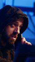 Vertical Hacker hiding in underground bunker, chatting with friend in telephone call, anxious after stealing data from victims using computer virus, scared about being caught by police, camera A close up video