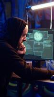 Vertical Malicious man hacking and talking on phone with partner, stealing credit card numbers, manipulating banking systems. Evil hacker runs dangerous code, chatting with friend in telephone call, camera B video