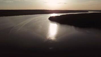 wide river is flowing at sunset in the summer. Sun's rays are reflecting in the water of the lake. Aerial view video
