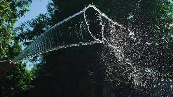 human's hands are holding a hose with water in the yard. Water are flowing by stream on the background of garden. Slow motion video