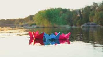 several multi-colored origami in the shape of ships are floating on the water in the lake in the evening on the background of the summer landscape video
