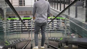 A man with a trolley on escalator in a hardware store, back view video