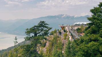 Sea to Sky Gondola on cliff with mountain range and forest view. A scenic observation deck perched on a cliff offers stunning views of a forested mountain range. video