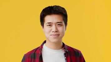Asian young man stands confidently, making a phone gesture with his hand while wearing a plaid shirt. The bright yellow background adds energy and a modern vibe to the composition. video