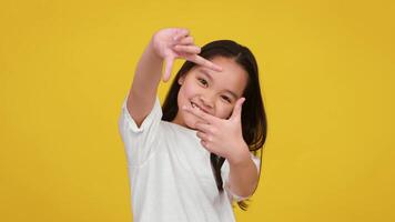 Asian young girl smiles and makes a playful hand gesture while standing against a vivid yellow backdrop. video