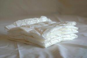 Stack of soft white quilted baby changing mats lying on white sheets photo