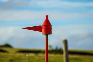 Red metal wind direction indicator pointing left on farm photo