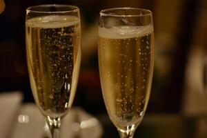 Two champagne flutes sparkling on a table in a warmly lit setting photo