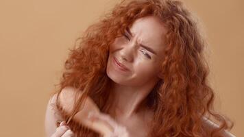 A woman with vibrant curly red hair is styling her hair, showing a playful expression while holding a section of her locks. She is in a studio with a warm, neutral background. video