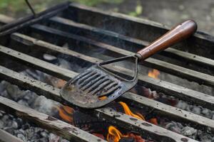 Old rusty metal spatula warming on top of barbecue grill photo