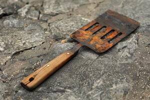 Rusty metal spatula with wooden handle resting on rocks photo