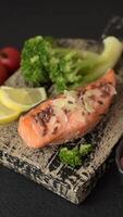 Grilled salmon with salt and spices, broccoli, tomatoes, rice on a dark concrete background video