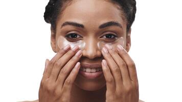 African American woman smiles while gently applying hydrating under-eye patches to her skin, showcasing her skincare routine in a bright, inviting atmosphere. video