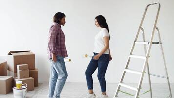 A couple is engaged in home improvement, walking around a room filled with cardboard boxes. One person is on a ladder while the other is organizing supplies, ready to paint their space. video
