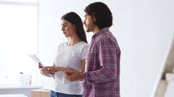 A man and woman are engaged in conversation while reviewing a document in a bright, airy room. They appear focused, with boxes visible in the background, suggesting a home setup. video