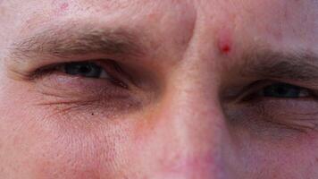 Close up to upset male face looking into camera with a disappointing sight. Upset facial expression of man with blue eyes. Unhappy gaze of despairing young guy. Slow motion video