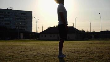 Professional footballer juggling soccer ball on stadium at sunset. Young man kicking ball at green field. Sportsman practicing tricks at meadow with sunlight at background. Freestyle football concept video