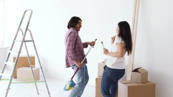 A couple enjoys decorating their new home, playfully laughing as one holds a paint roller. They are surrounded by moving boxes and a ladder, preparing to create a fresh space. video