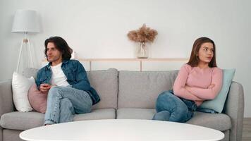 A young couple sits on opposite ends of a couch, visibly upset and in silence. Tension fills the air as they avoid eye contact, suggesting an unresolved conflict. video