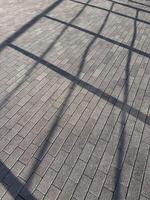 Shadow of metal fence on grey brick pattern pavement. Abstract background and texture. Sunlight,light and shadow concept photo