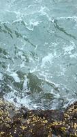 Close-up of surge of waves on rocky shore. Clip. Beautiful waves with splash roll on stones of seashore. Beautiful splashes of waves crashing on rocks on cloudy day video