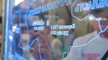 A man reviews a map on a computer, collaborating with another on a glass wall video